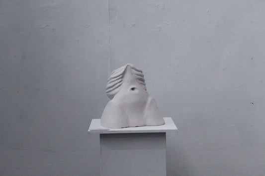 Exposed ceramic sculpture on a white pedestal against a gray background, showcasing unique texture and design.